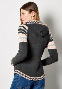 Sudadera gris con patrón de zigzag en rosa y negro en las mangas y el dobladillo. Diseñada con un borde inferior redondeado y tela texturizada.