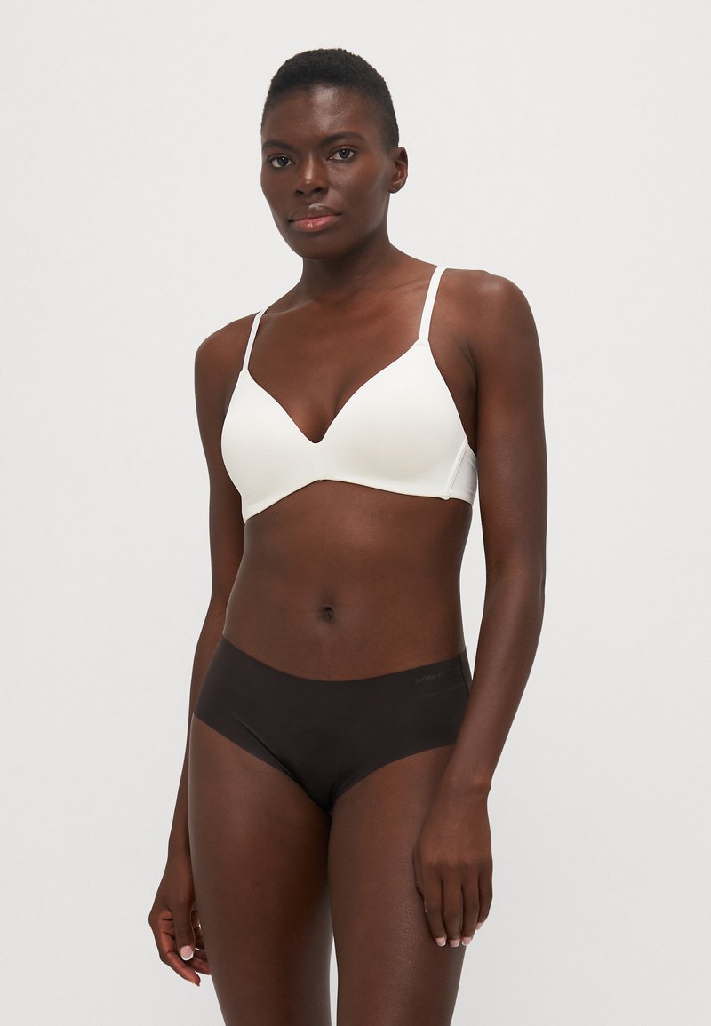 Witte draadloze bh met een V-vormige halslijn, gecombineerd met zwarte boyshorts. Beide kledingstukken hebben een gladde textuur en een minimalistisch ontwerp.