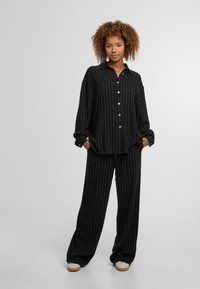 Čierna košeľa na gombíky a zodpovedajúce široké nohavice s bielymi vertikálnymi pruhmi. Mäkka a štruktúrovaná tkanina; voľný strih s klobúkovým výstrihom.