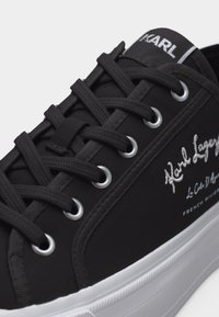 Μαύρο αθλητικό παπούτσι Karl Lagerfeld με λευκό κεντημένο λογότυπο, μαύρα κορδόνια που περνούν από μεταλλικά ροδέλες και λευκή καουτσούκ σόλα.