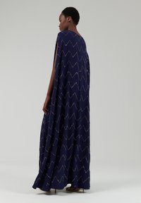 Navy Maxi-Kleid mit lockerer Silhouette, das von Zickzackmustern mit kleinen Perlen akzentuiert wird, sowie seitlichen Schlitzen für einen fließenden Effekt.