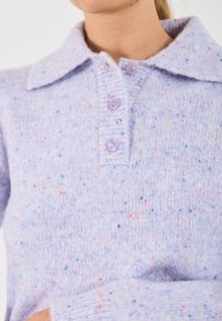 Maglione a maglia lilla con colletto, caratterizzato da macchie pastello, tre bottoni e una texture morbida.