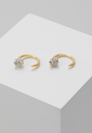 Paire de boucles d'oreilles créoles ouvertes en or, chacune avec une petite pierre précieuse claire en forme d'étoile sertie sur six griffes, exposée sur une surface blanche.