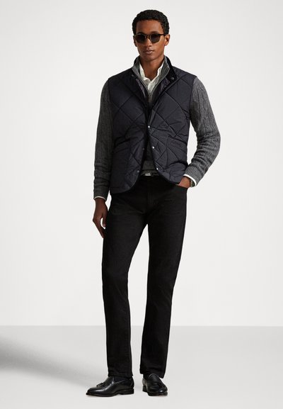 Prešívaná námornícka vesta cez sivý sveter s vrkočovým vzorom, v kombinácii s čiernymi úzkymi nohavicami a čiernymi mokasínami. Doplnky zahŕňajú slnečné okuliare.