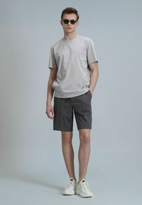 T-shirt gris à manches courtes avec un col rond, associé à un short gris avec des coutures avant. Modèle portant des baskets blanches et des lunettes de soleil.