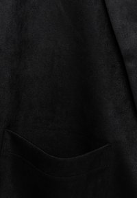 Gros plan sur un tissu noir à texture douce avec une couture de poche visible dans la partie inférieure.