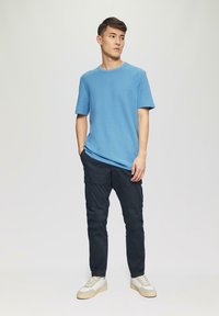 Blauwe katoenen T-shirt met ronde hals, gecombineerd met donkere cargobroek met zijzakken en witte sneakers met beige accenten.
