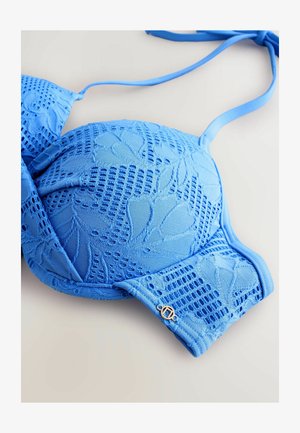 Sinine pitsbikiini ülemine osa lillemustriga ja õhukeste õlapaeltega heledal pinnal.