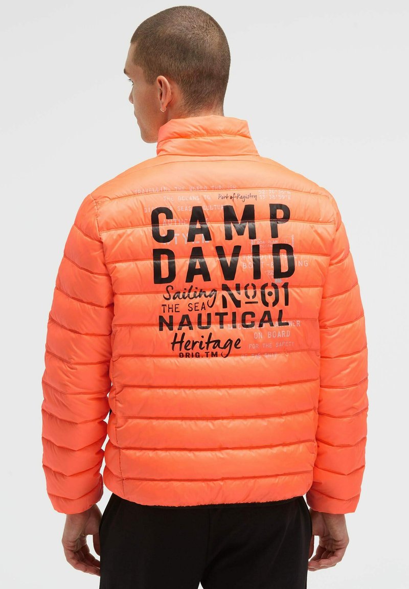 Orangefarbene Steppjacke mit gestepptem Design. Auf der Rückseite befinden sich schwarze Schriftzüge "CAMP DAVID" und nautisch inspirierte Akzente.