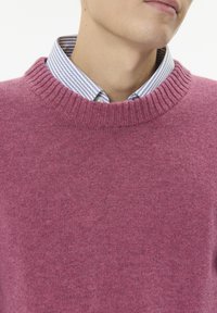 Rózsaszín kötött pulóver bordázott nyakkivágással, kék-fehér csíkos galléros ingre rétegezve. Sima textúra és laza, hétköznapi dizájn.