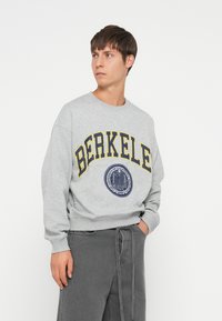 Gray sweatshirt featuring yellow and navy text reading "BERKELE" and a circular university seal. Long sleeves with ribbed cuffs.