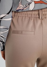 Beige, hooggetailleerde broek met een elastische tailleband, voorzien van een gestikte zak aan de achterkant en een gladde, licht getextureerde stof.