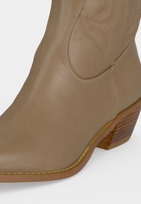 Καφέ δερμάτινη καουμπόικη μπότες με ραμμένα διακοσμητικά σχέδια και στοιβαγμένο ξύλινο τακούνι.