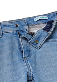 Jeans de mezclilla azul claro con corte recto, que cuentan con cremallera, cierre de botón y detalles de costura en contraste. Etiqueta de la marca visible.