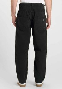 Zwarte katoenen cargobroek met een losse fit, twee achterzakken en een klein merklabel op de rechterzak.