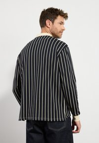 Marineblauw en crèmekleurig gestreept shirt met lange mouwen en een ronde hals, voorzien van zijsplitten en een ontspannen pasvorm. Gemaakt van zacht katoen.
