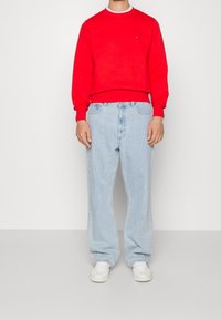 Rode crewneck trui met geribbelde manchetten, gecombineerd met lichtblauwe losse spijkerbroeken en witte sneakers. Eenvoudig ontwerp met minimale merkaanduiding.