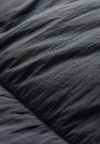 A fekete ripstop szövet ráncos textúrájú, sima felülete finom, szabálytalan redők és gyűrődések által megszakított.