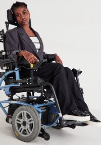 Ηλεκτρικό αναπηρικό αμαξίδιο με μπλε σκελετό, μαύρη έδρα και μεγάλες ρόδες. Άτομο με μαύρη ριγέ στολή και σακάκι, καθισμένο με αυτοπεποίθηση.
