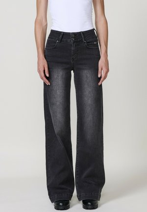 Jeans de mezclilla negros de pierna ancha con un acabado desteñido, que cuentan con una bragueta de botones, bolsillos delanteros y detalles de costura sutiles. Textura suave.
