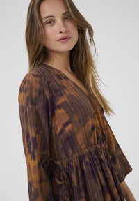 Fialová a hnedá tie-dye šaty s V-výstrihom, dlhými zvonovými rukávmi a sťahovacím pásom. Ľahká, textúrovaná tkanina.