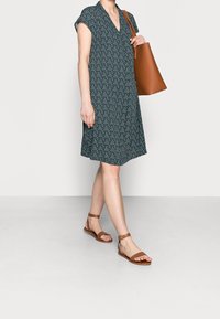 Tmavě zelené šaty s výstřihem do V, krátkými rukávy a vzorem malých bílých vertikálních pruhů, doplněné hnědými koženými sandály a kabelkou typu tote.