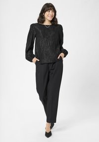 Bluză neagră, texturată, cu mâneci lungi și bufante. Asortată cu pantaloni negri, cu talie înaltă, și pantofi cu vârful ascuțit, cu buline.