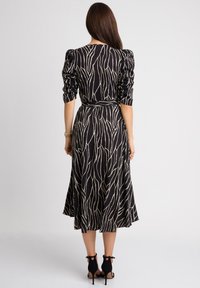 Czarna sukienka z kremowym, abstrakcyjnym wzorem w liście, długimi bufkowymi rękawami, dopasowaną talią i rozkloszowanym dołem. Nosi się ją z czarnymi sandałami na obcasie.