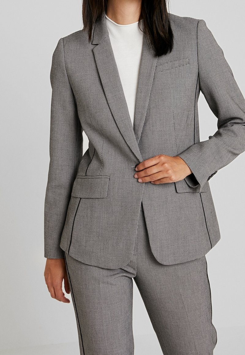Grau kariertes Blazer mit Reverskragen, zwei Vorderaschen und taillierter Passform. Textilstruktur und minimalistische Designdetails.