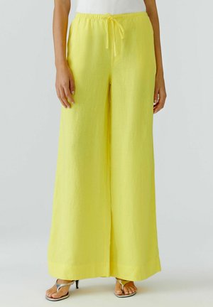 Person trägt leuchtend gelbe, weit geschnittene Hose mit Kordelzug in der Taille, kombiniert mit silbernen offenen Sandalen mit Absatz.