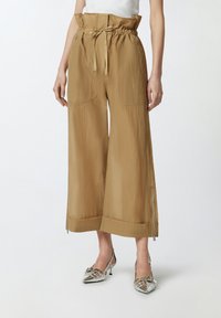 Kakhi široke hlače s teksturiranom završnom obradom, elastičnim pojasom, zatvaranjem na vezicu i bočnom zip zatvaranjem. Uparen s srebrnim potpeticama.