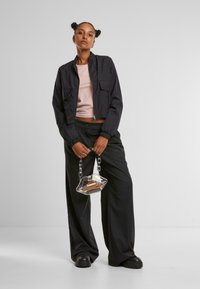 Black cropped jacket with elastic cuffs, lightweight fabric, two front pockets; paired with loose black trousers and a clear bag with a chain handle.