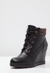 Ces bottines noires en simili cuir disposent d'une semelle compensée, d'un laçage avant et d'un rebord rembourré marron. Finition texturée avec des œillets métalliques et une conception robuste.