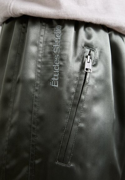 Shorts en satin vert olive avec un logo brodé, une poche latérale zippée et une texture lisse.