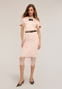 Blusa in raso rosa chiaro con colletto a contrasto nero, abbinata a una gonna a matita con bordo in pizzo e decolletè lucidi a punta.