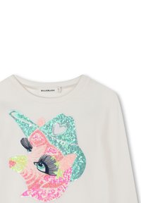 Chemise blanche à manches longues avec un visage de licorne en sequins portant un chapeau de cowboy turquoise avec un détail en forme de cœur.