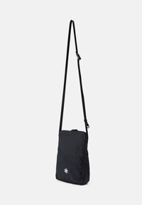 Borsa a tracolla nera in nylon con una forma rettangolare slim, tracolla regolabile e chiusura con zip frontale. Presenta un accento con logo bianco.