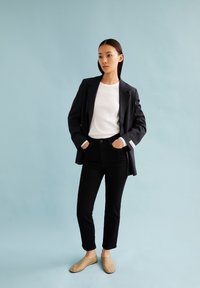 Blazer navy con rayas sobre una camisa blanca de canalé, jeans negros y zapatos tipo slip-on color beige claro. Texturas suaves y ajuste entallado.
