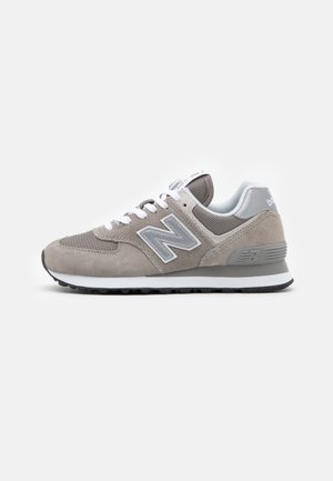 Grå og hvide New Balance-sneakers med ruskind og mesh-paneler, hvide snørebånd og tekstureret gummisål på en hvid baggrund.