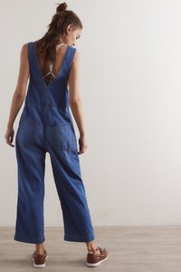 Trapere od trapera s dubokim V-izrezom na leđima, širokim nogavicama i prednjim džepovima, uparen s smeđim cipelama s ukrasnim vezicama. Glatka, teksturirana tkanina.