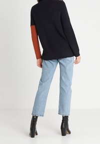 Pull en tricot bleu marine avec des manches couleur rouille, associé à un jean droit bleu clair et des bottes à talons noires.
