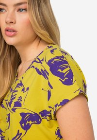 Top amarillo de manga corta con un audaz patrón abstracto morado, con cuello redondeado y textura de tela suave.