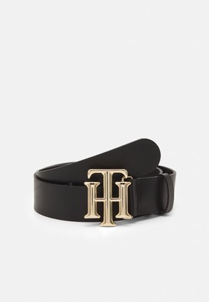 Ceinture en cuir noir avec une boucle en métal doré présentant les lettres T et H superposées, enroulée sur un fond blanc.
