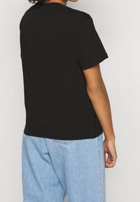 Svart bomullströja med kort ärm, rund halsringning och en avslappnad passform, i kombination med ljusblå denimbyxor.