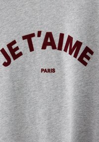Grå bomulds sweatshirt med bordeaux tekst, der læser "JE T'AIME" i en bue ovenfor og "PARIS" nedenfor, med en blød tekstur.