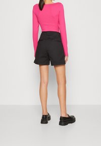 Pantaloni corti neri con una vestibilità comoda, abbinati a un top aderente a maniche lunghe di un vivace rosa brillante. I dettagli includono una cintura con passanti e tasche posteriori.