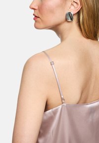 Light pink satin camisole with adjustable straps and a smooth texture, paired with a large, shiny, silver earring.