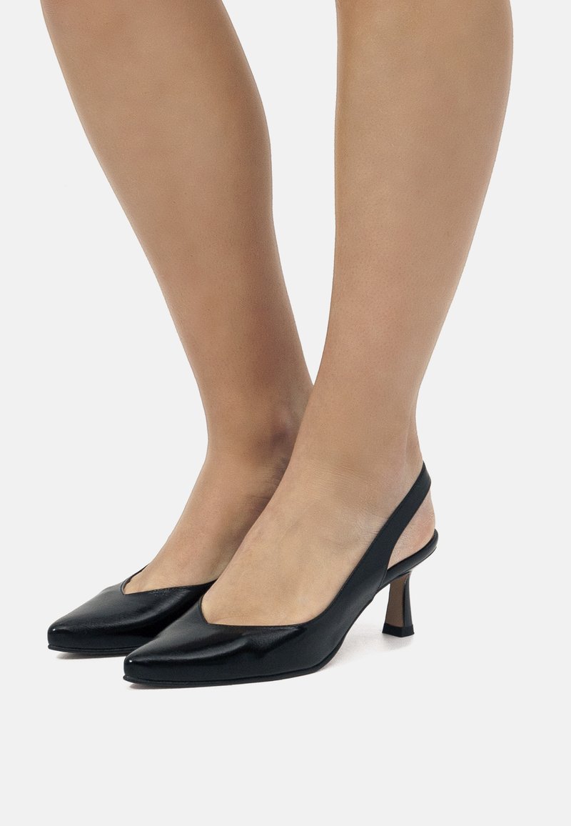 Zapatos de tacón negro tipo slingback con punta afilada y tacón bajo. Material de cuero liso con un diseño elegante y un sutil corte en V en la parte superior.
