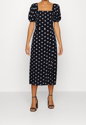 Black midi dress with white floral print, square neckline, puff sleeves, and a high slit. Paired with black ankle strap heels.