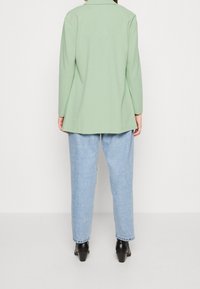 Mintgrön långärmad blazer med rak skärning, i kombination med ljusblå slitna jeans och svarta klackstövlar.